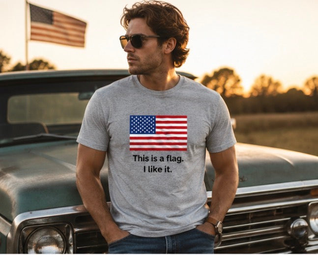 A man wearing a heather gray t-shirt with a graphic of the American flag and the text 'This is a flag. I like it.