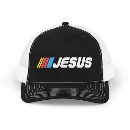 A black and white trucker hat with a black front panel and white mesh back. The front panel features a colorful embroidered logo with yellow, red, and blue stripes followed by the word 'JESUS' in white.