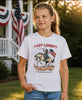 Young girl wearing a 'Lady Liberty' t-shirt with a horse and American flag design, standing outdoors.