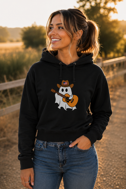 A woman wearing a black hoodie with a cartoon ghost playing guitar graphic, standing outdoors on a dirt path during warm golden hour sunlight.