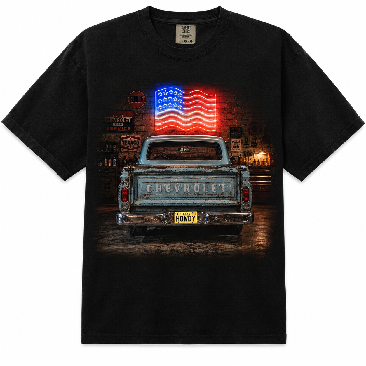 A black short-sleeve graphic t-shirt featuring a vintage light blue Chevrolet pickup truck from the rear, with a glowing red, white, and blue American flag on the tailgate, set against a dark street scene.