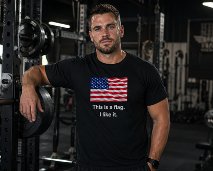 A man in a gym wearing a black t-shirt with a graphic of the American flag and the text 'This is a flag. I like it.'