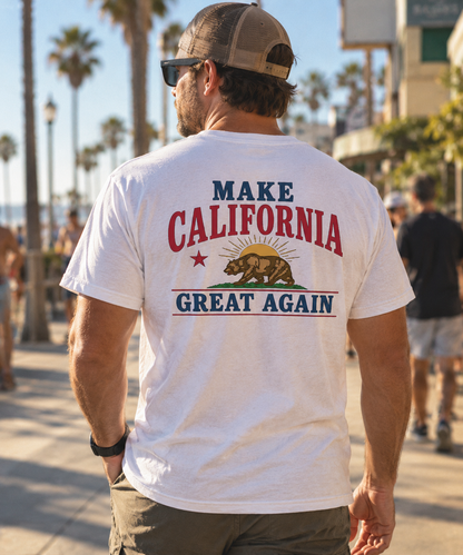 A man viewed from behind wearing a white graphic t-shirt with 'MAKE CALIFORNIA GREAT AGAIN' and the California grizzly bear design printed on the back, set against a sunny outdoor boardwalk background.