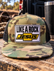 “Camo flat bill trucker hat with black mesh sides and a white Like a Rock Jesus patch with yellow detailing.”