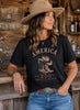 Woman wearing a black t-shirt with 'America 250' design in a rustic setting.
