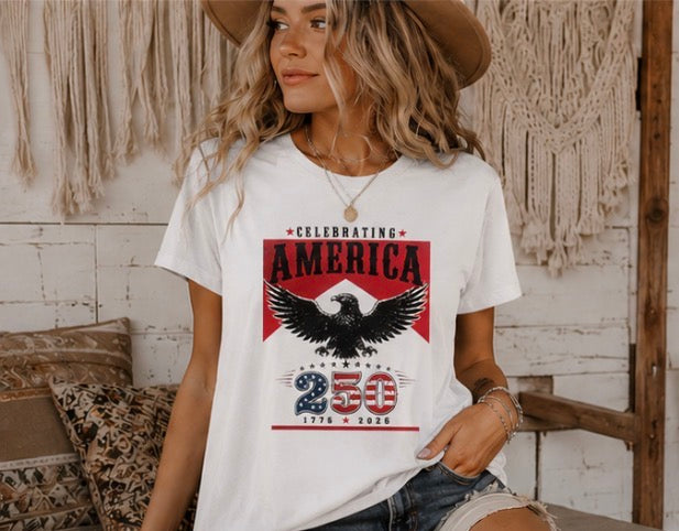 Woman wearing a white t-shirt with an eagle graphic and text, standing in a rustic indoor setting.