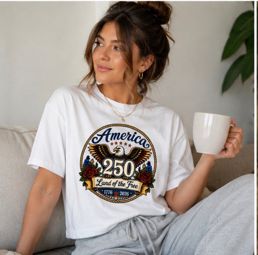 Woman wearing a white t-shirt with 'America 250' design, holding a mug indoors.