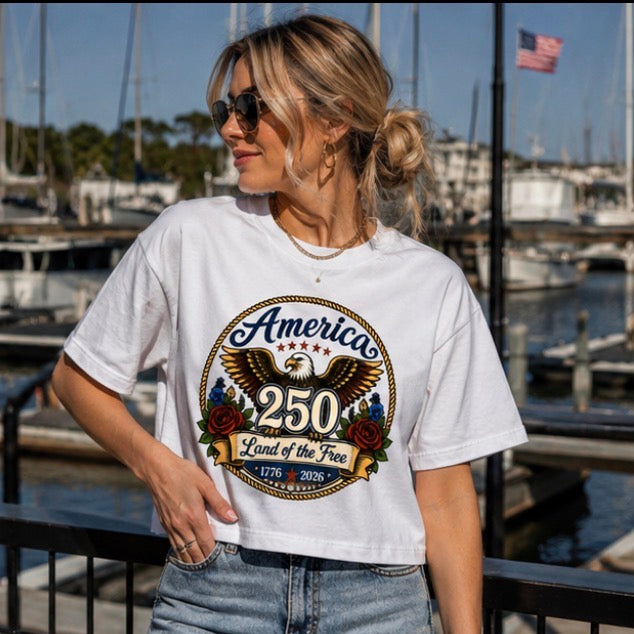 Woman wearing a white t-shirt with an eagle graphic and text by a marina.