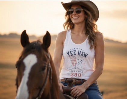 Woman in a 'Yee Haw' tank top sitting on a horse in a field with a sunset.