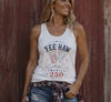 Woman wearing a white tank top with 'Yee Haw America 250' design against a wooden background