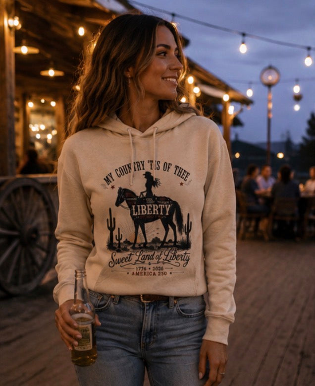 Woman wearing a hoodie with a desert-themed design, holding a drink outdoors.