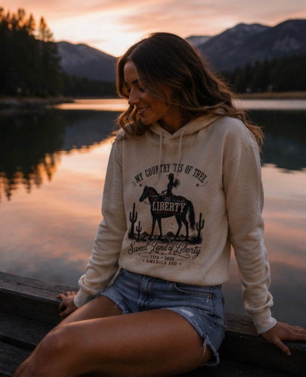 Woman wearing a hoodie with a graphic design sitting by a lake at sunset.