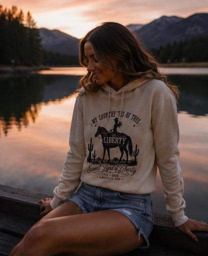 Woman wearing a hoodie with a graphic design sitting by a lake at sunset.