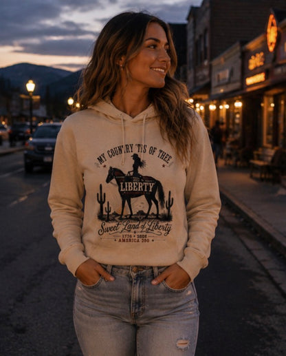 Woman wearing a hoodie with a graphic design of a cowboy and text, standing on a street at dusk.