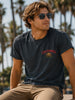 Man wearing a black t-shirt with 'California' and a bear graphic, sitting outdoors with palm trees in the background.