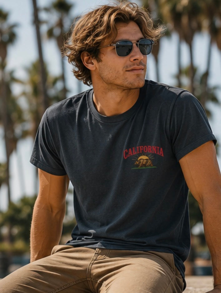 Man wearing a black t-shirt with 'California' and a bear graphic, sitting outdoors with palm trees in the background.