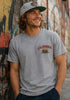 Man wearing a gray 'California' t-shirt with a bear graphic against a graffiti-covered wall.
