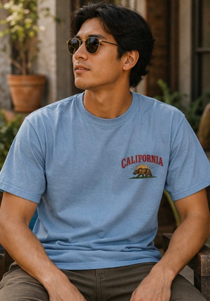Man wearing a blue t-shirt with 'California' and a bear graphic, sitting outdoors.