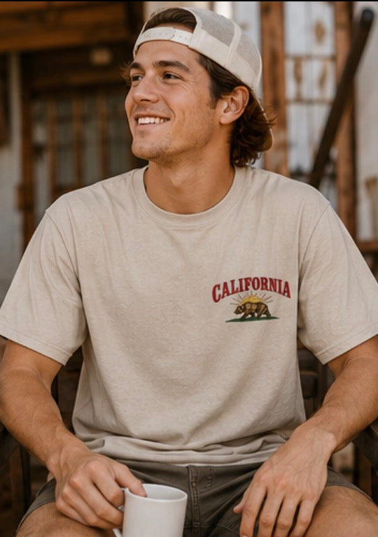 Man wearing a 'California' t-shirt with a bear graphic, sitting outdoors.