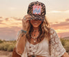 Woman wearing a leopard print cap with 'OH MY STARS' text, sitting outdoors at sunset.