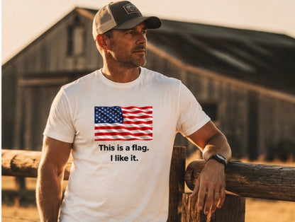A man wearing a white graphic t-shirt with an American flag print and the text 'This is a flag. I like it.
