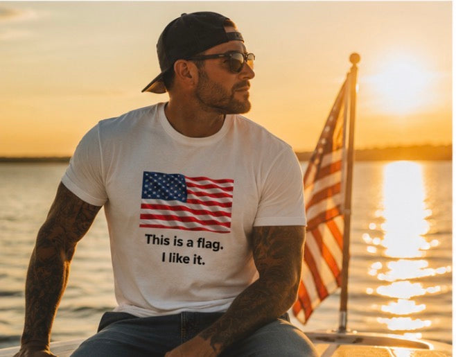 A man wearing a white graphic t-shirt with an American flag print and the text 'This is a flag. I like it.