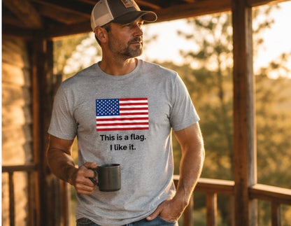 A man wearing a heather gray t-shirt with a graphic of the American flag and the text 'This is a flag. I like it.