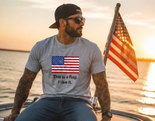 A man wearing a heather gray t-shirt with a graphic of the American flag and the text 'This is a flag. I like it.