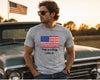 A man wearing a heather gray t-shirt with a graphic of the American flag and the text 'This is a flag. I like it.