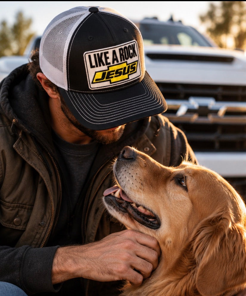 “Man wearing a black and white Like a Rock Jesus trucker hat while petting a golden retriever beside a truck.”

