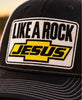 “Close-up of the Like a Rock Jesus embroidered patch in black, white, and yellow on a black trucker hat.”
