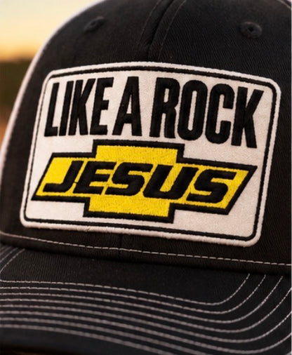 “Close-up of the Like a Rock Jesus embroidered patch in black, white, and yellow on a black trucker hat.”