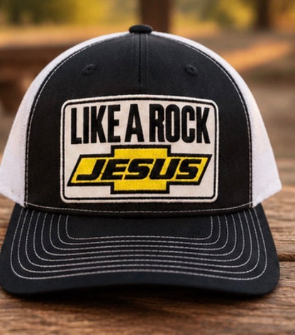 “Front view of Like a Rock Jesus trucker hat with white mesh sides, displayed on a wooden table.”