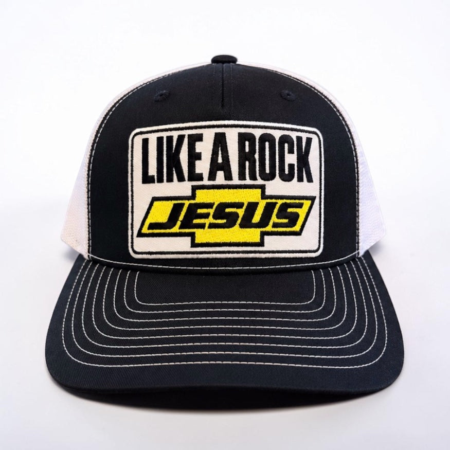 “Front view of black and white Like a Rock Jesus trucker hat with embroidered patch and white stitching on the bill.”
