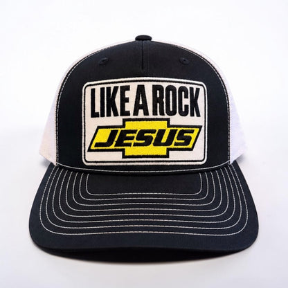 “Front view of black and white Like a Rock Jesus trucker hat with embroidered patch and white stitching on the bill.”
