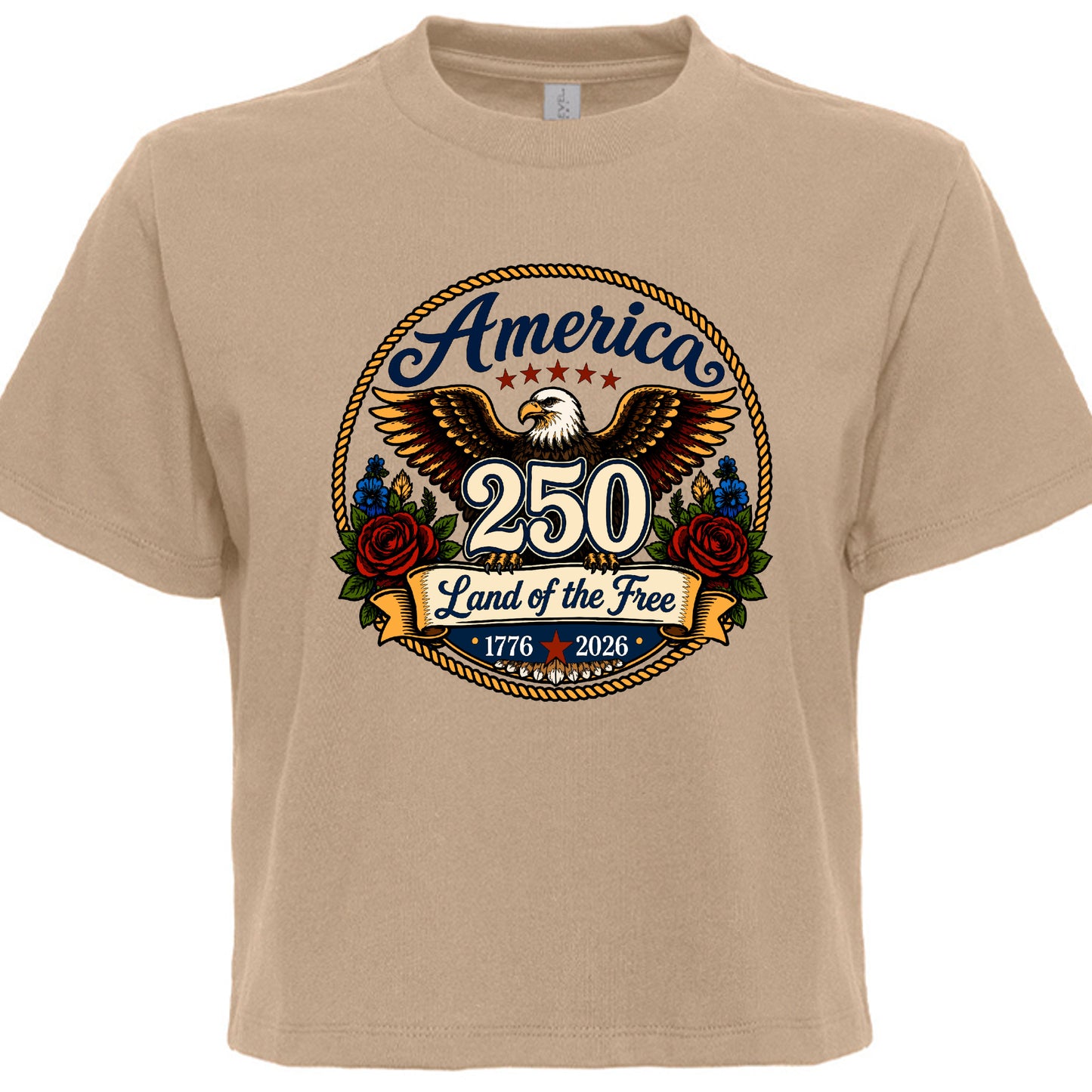 Women's tan patriotic tee with vintage tattoo style circular graphic featuring golden eagle red roses gold rope border and America 250 Land of the Free 1776 to 2026 design
