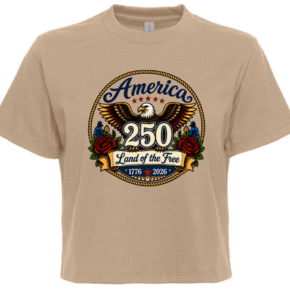 Women's tan patriotic tee with vintage tattoo style circular graphic featuring golden eagle red roses gold rope border and America 250 Land of the Free 1776 to 2026 design
